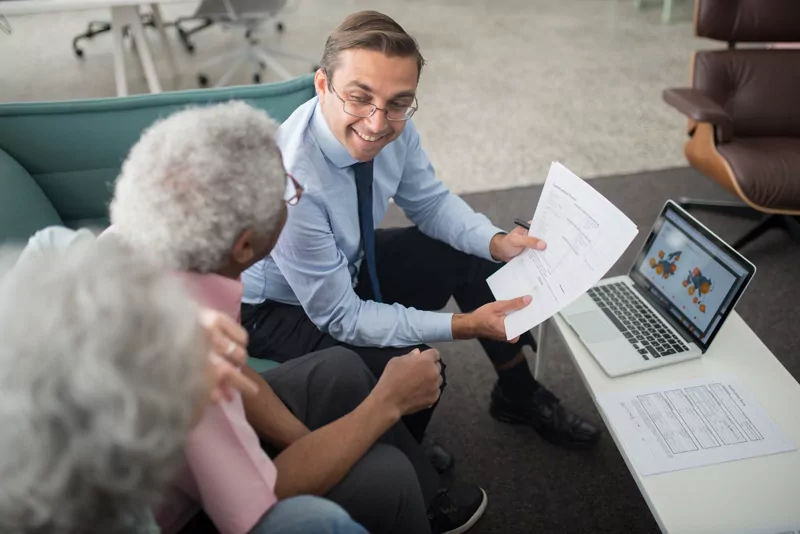An adviser reviews paperwork with two older clients beside a laptop